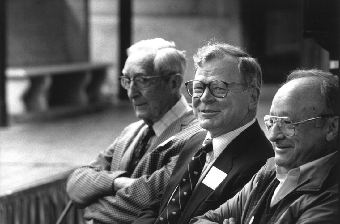 Historical black and white photo of three men, all wearing suits and glasses