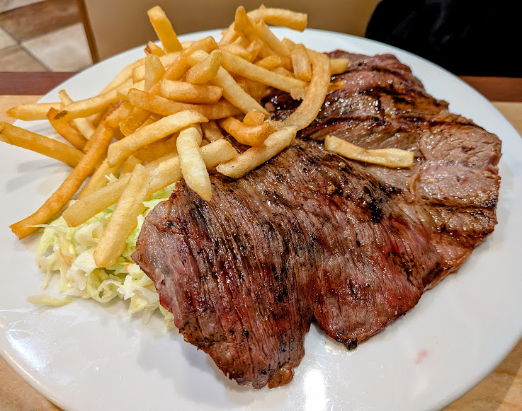 A plate with grilled steak, French fries, and shredded cabbage on a white dish.