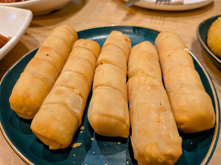 Five golden-brown fried spring rolls arranged side by side on a dark green plate.