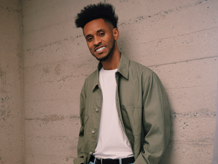 a man poses against a wall smiling