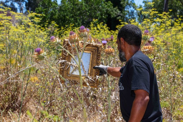 Community member Rafa Rivera picks up a mirror while cleaning up a vacant lot at the corner of MacArthur Boulevard and 83rd Avenue in Oakland, Calif., on Thursday, July 23, 2026. (Ray Chavez/Bay Area News Group)