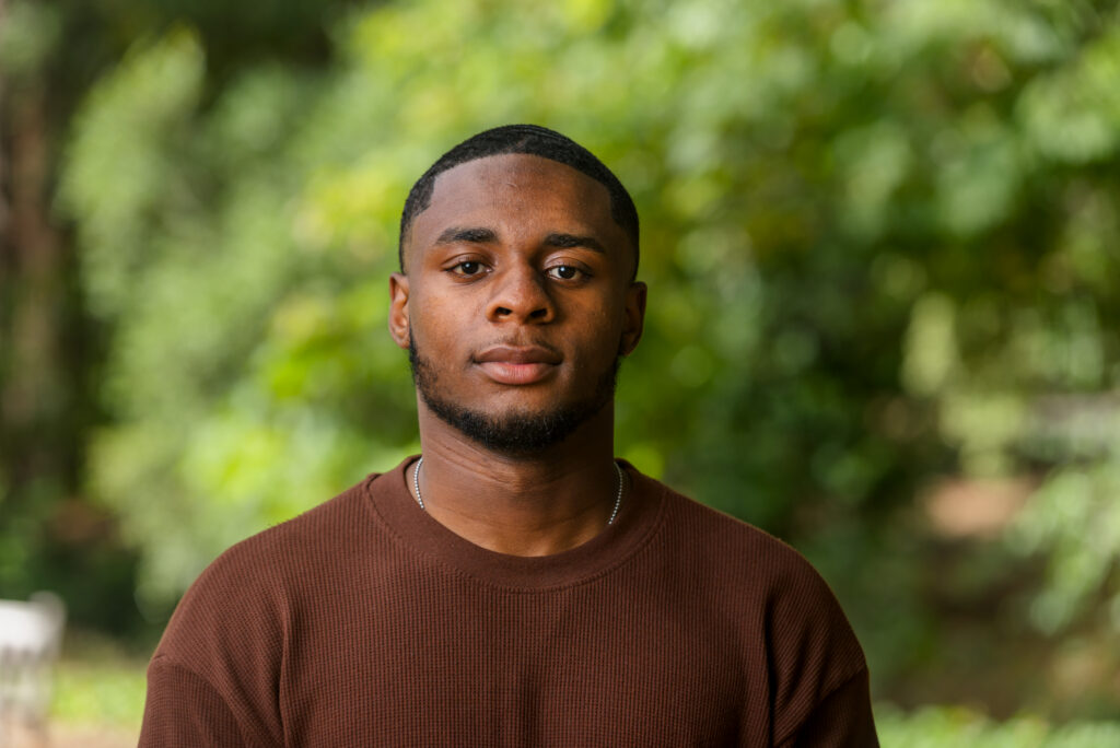 Student Evan Fewell faces the camera. The background is out of focus green foliage.
