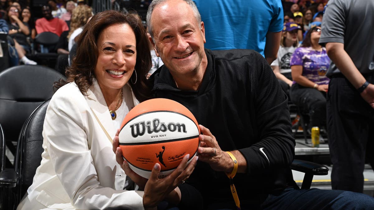 Kamala Harris and Doug Emhoff sit in the arena stands at a basketball game.