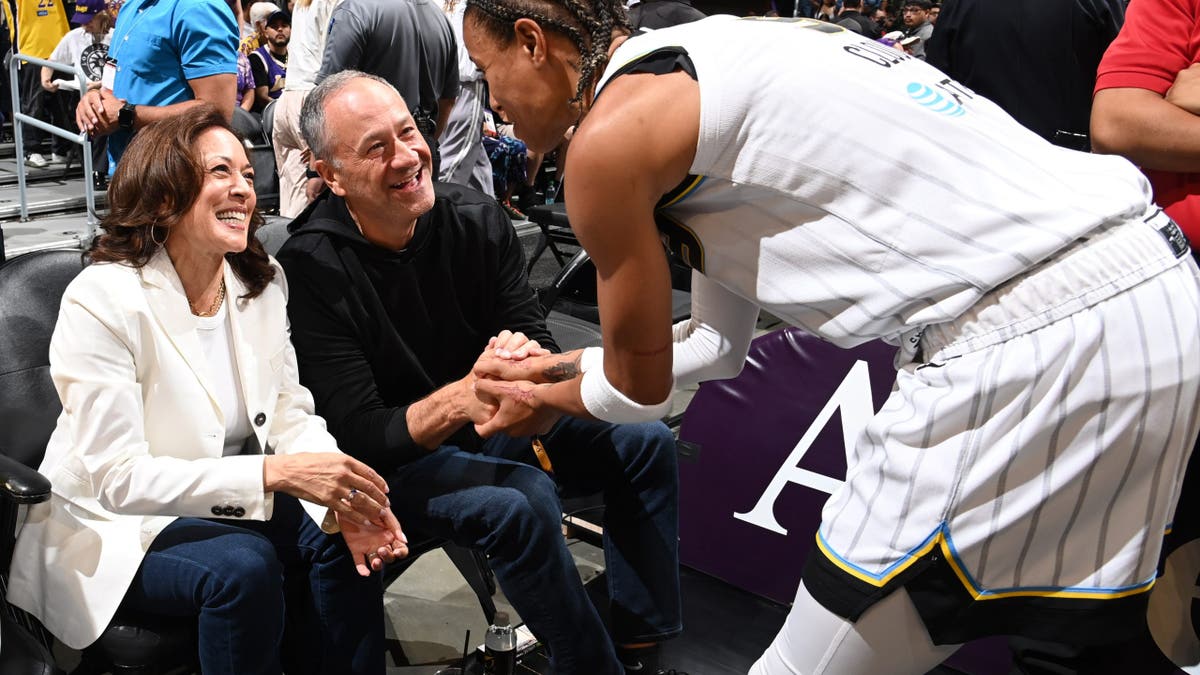 Natasha Cloud shakes hands with Kamala Harris and Doug Emhoff during a basketball game in Los Angeles.