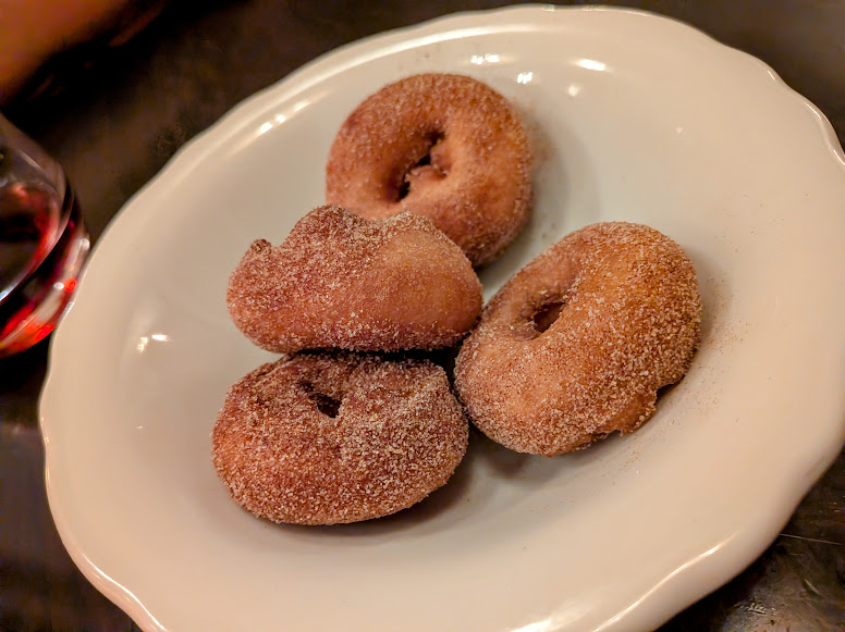 Four cinnamon sugar donuts are arranged on a white plate, set on a dark surface.