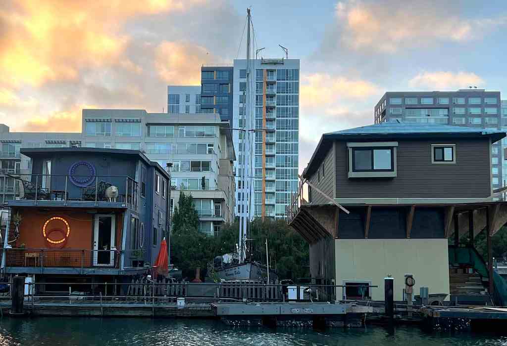 Two houseboats with apartment towers and the sunset in the background.