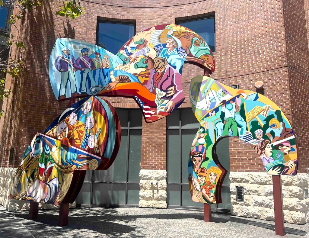 A multicolored sculpture in front of a brick building.