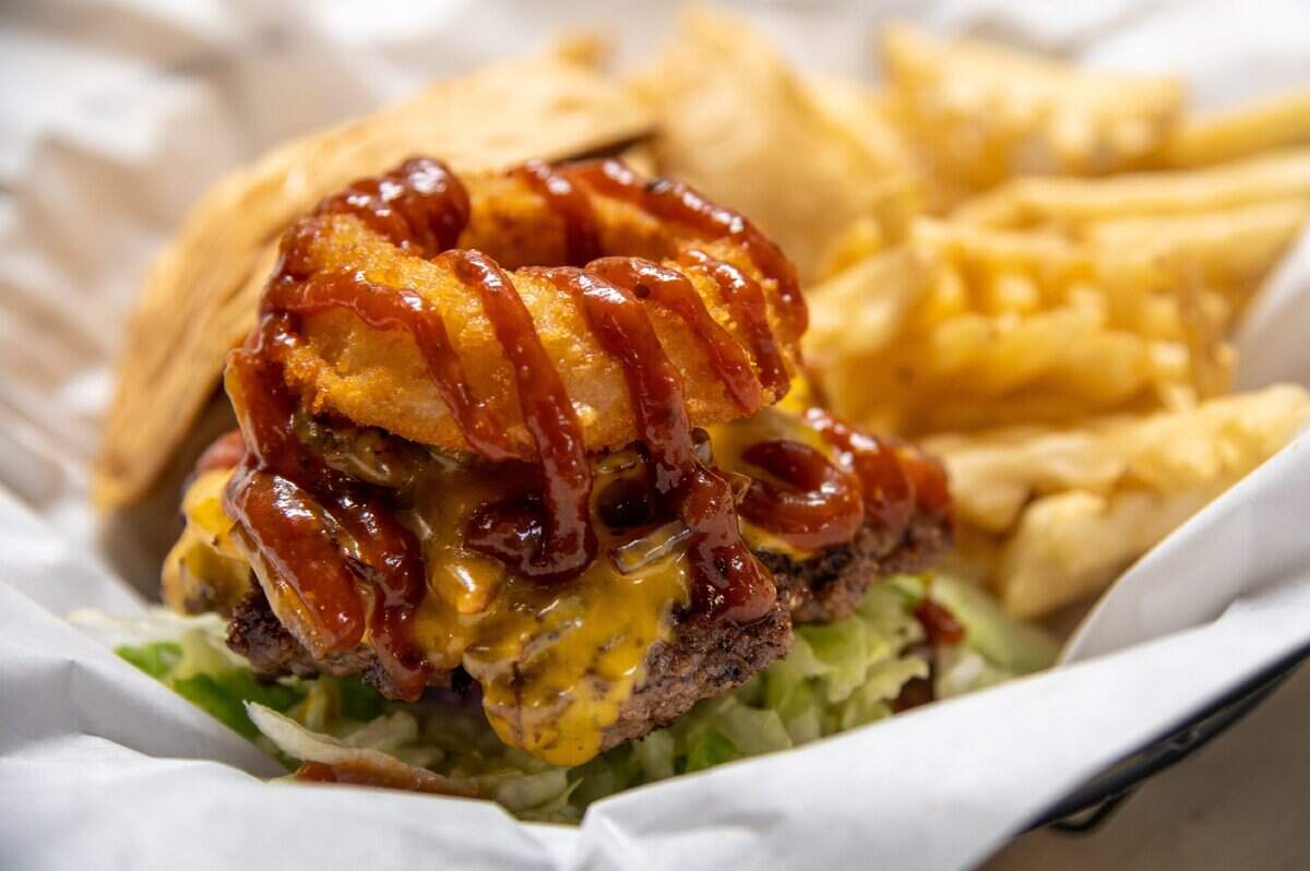 A "Western Burger" made of thick-cut cherrywood smoked bacon, onion ring, BBQ sauce, medium sharp cheddar cheese is ready to be served with criss-cut fries at Skip's Kitchen in 2021.