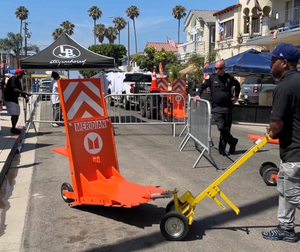 A person pushes a large orange barrier on a street next to a police officer.