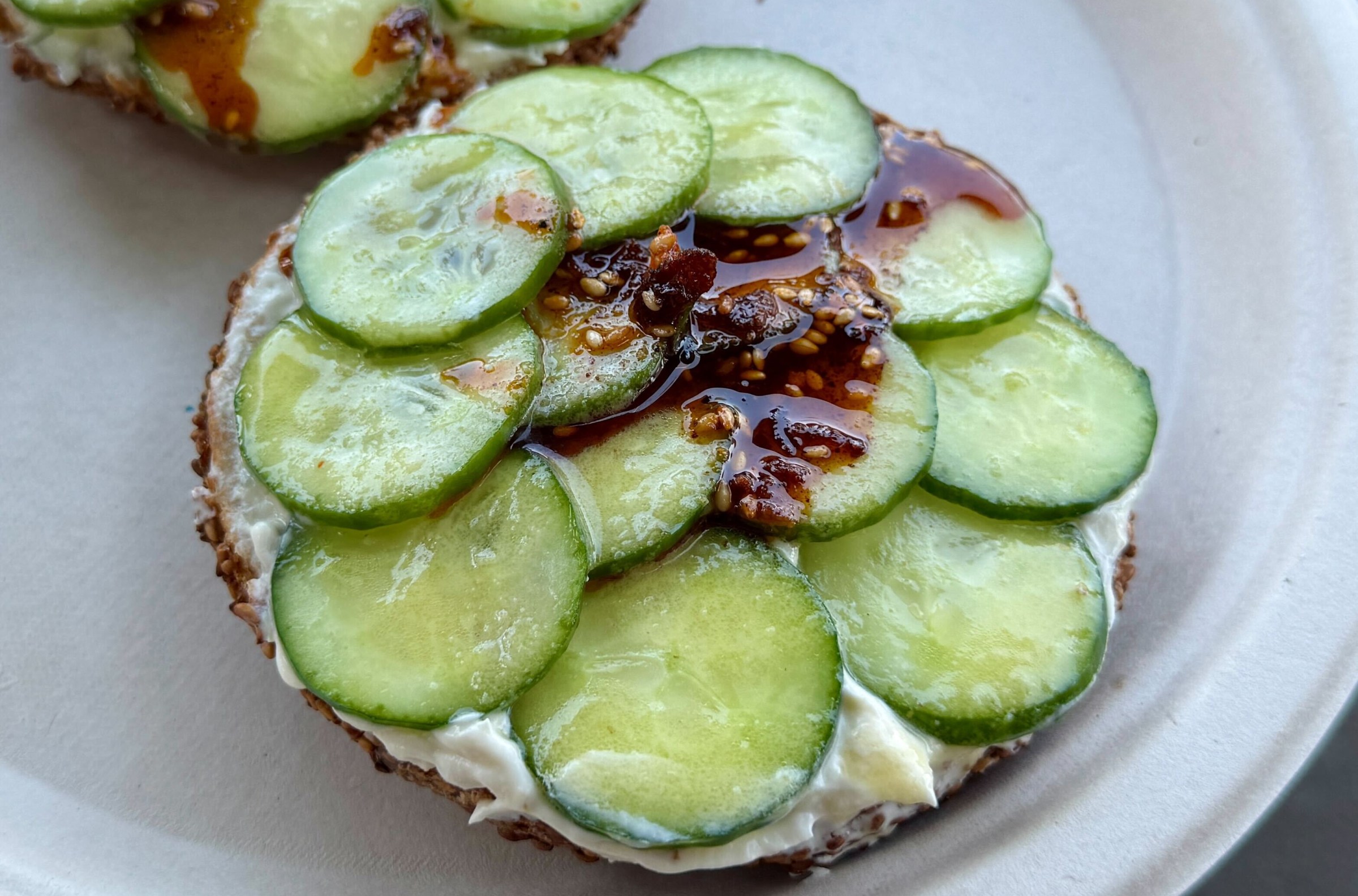 A bagel topped with cream cheese and sliced cucumbers covered in chile crisp from Mustard’s Bagels.
