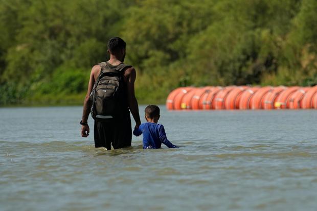 Migrants walk past large buoys being used as a floating border barrier.