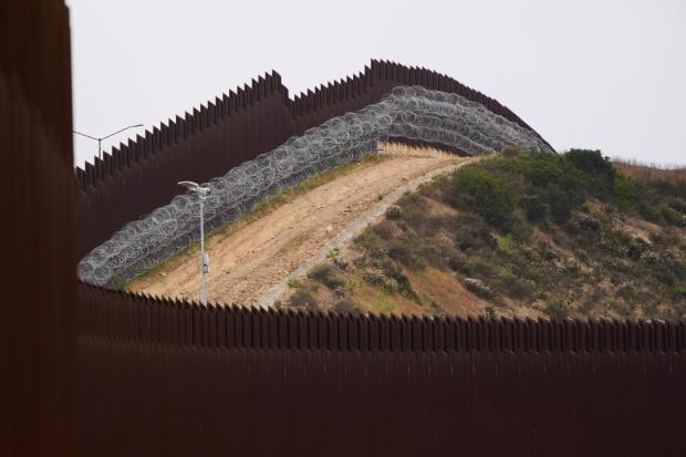 Concertina wire lines the interior of a border wall.