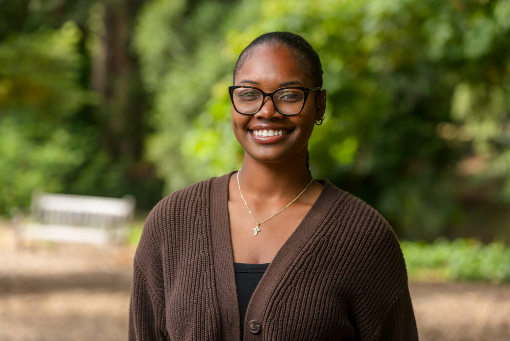 Joy Rutledge smiling into the camera with a fuzzy background of green vegetation