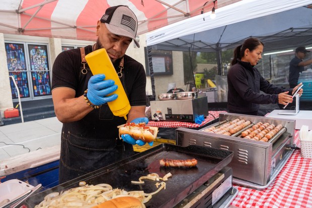 A vendor known as "Jesus the Hot Dog Guy" applies mustard to a hot dog during the Valley Foodzilla food festival on Macneil Street in San Fernando, California. Los Angeles is known for its iconic LA Street dogs. (Photo by Mark Savage, Contributing Photographer)