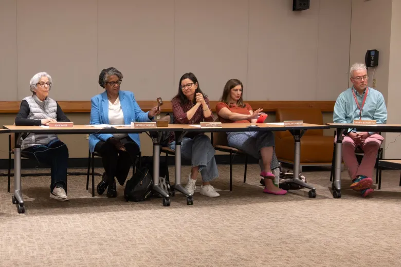Five people sit at a row of tables in a government meeting