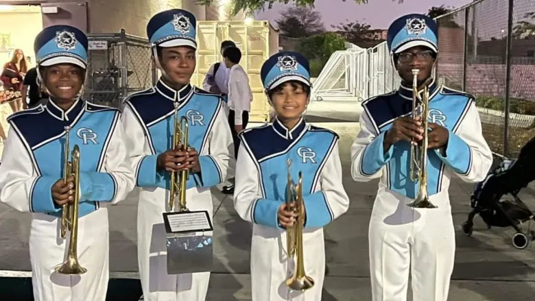 Four young band members in white and blue uniforms holding brass instruments.