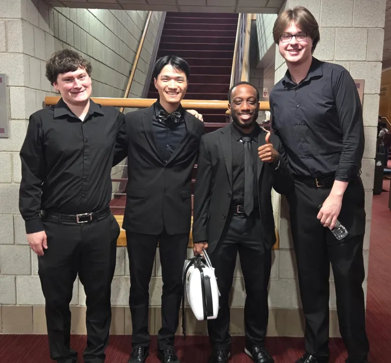 Four people in black formal attire smiling in a hallway.
