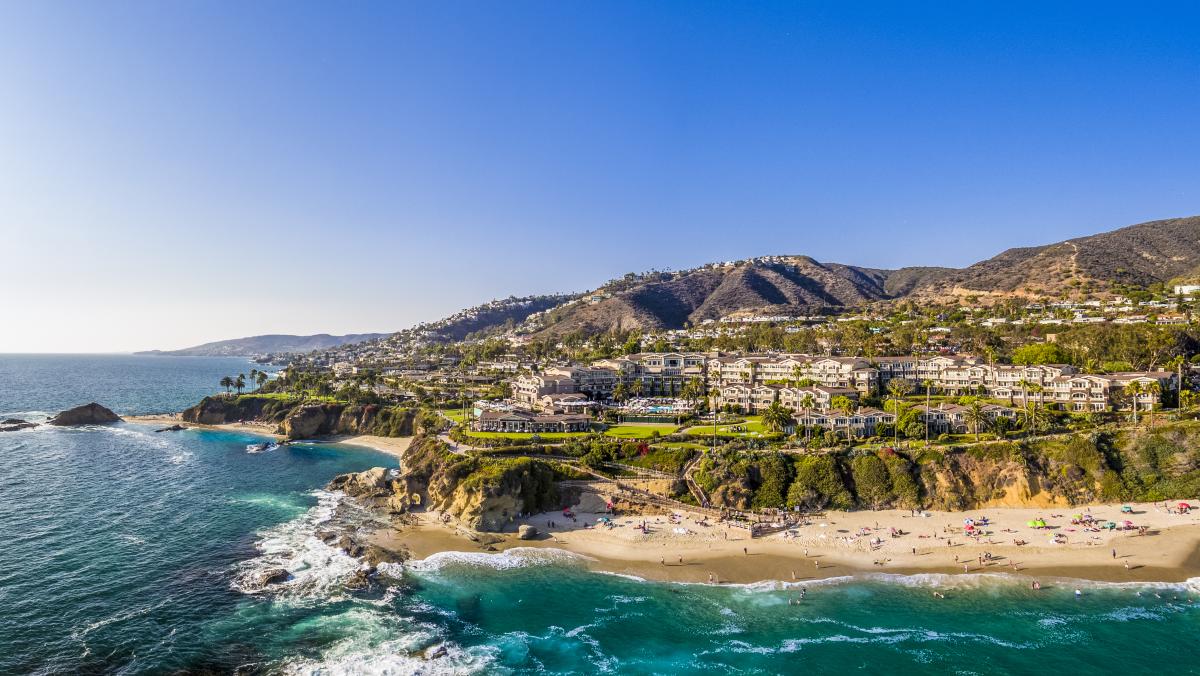 Panoramic view of Montage Laguna Beach resort with private beach access, golden sand, turquoise water, and clear California skies.