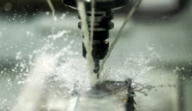 A CNC machine drilling into metal, with coolant fluid spraying around the cutting tool.