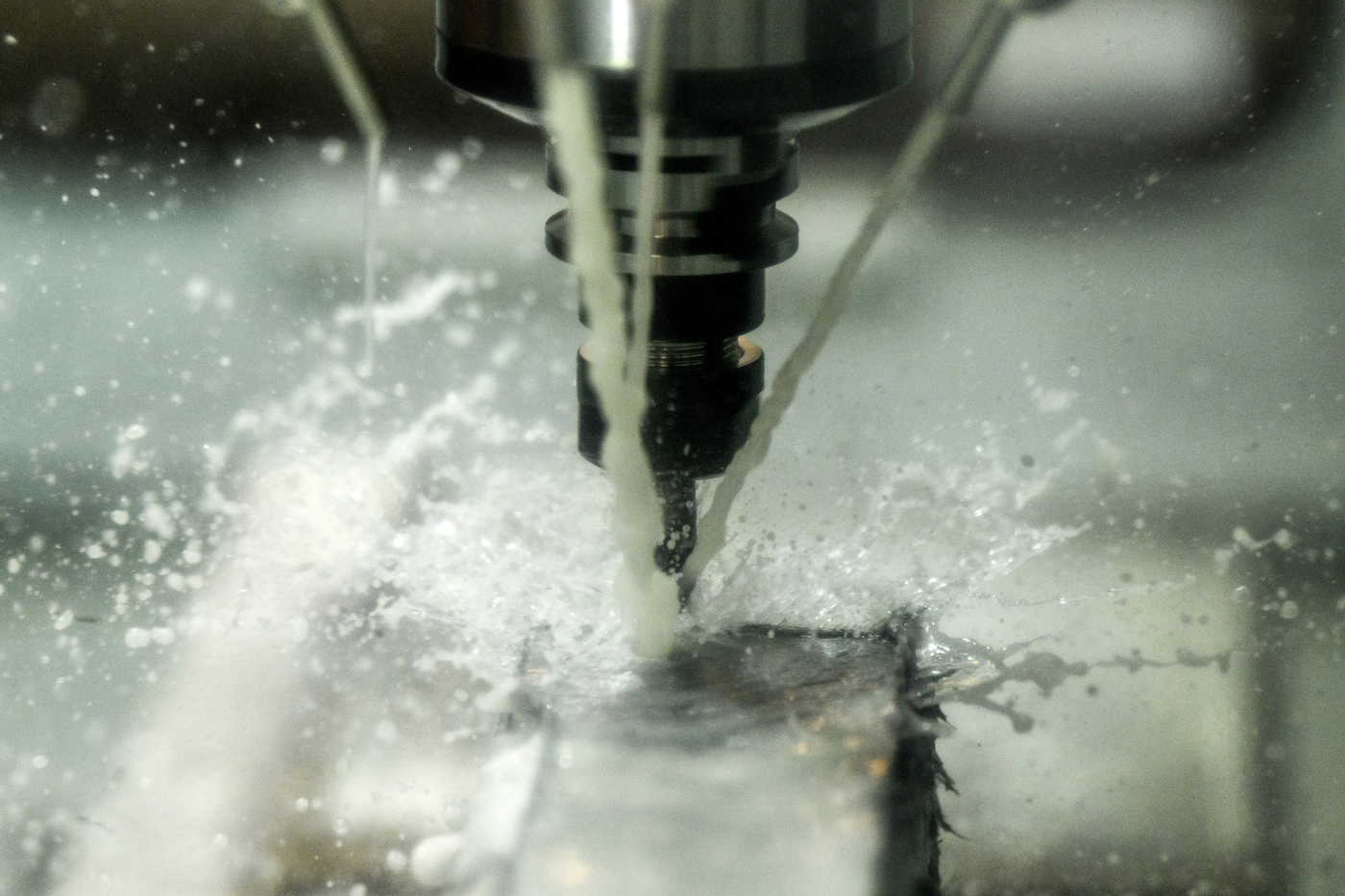 A CNC machine drilling into metal, with coolant fluid spraying around the cutting tool.