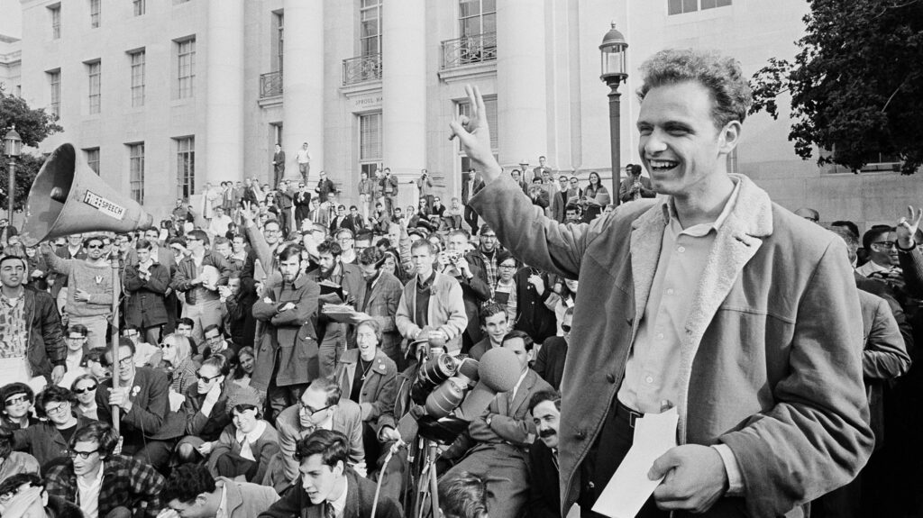 Mario Savio, a leader of the Free Speech Movement in 1960s Berkeley, flashes a peace sign with hundreds of students on the steps behind him on the steps of Sproul Hall.