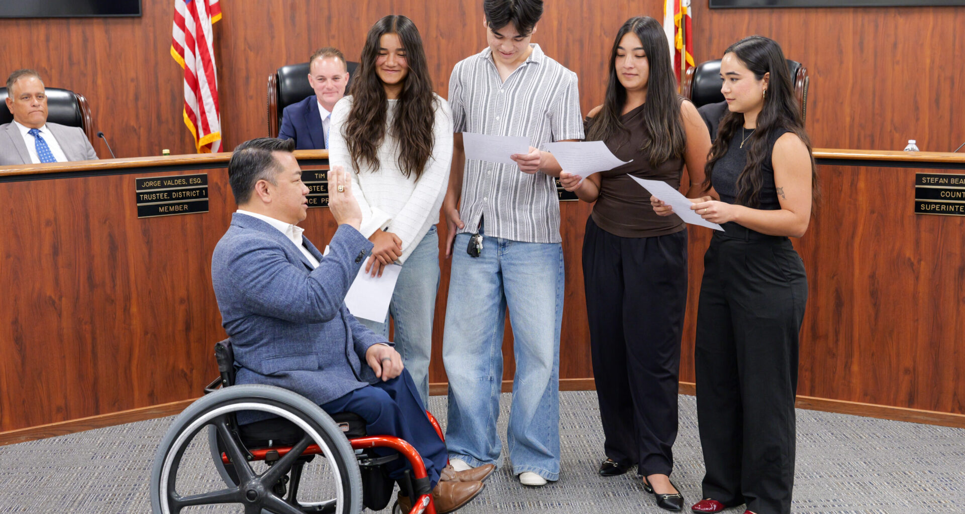 Dr. Stefan Bean raises his right hand while his four children administer the oath of office during an Orange County Board of Education meeting.