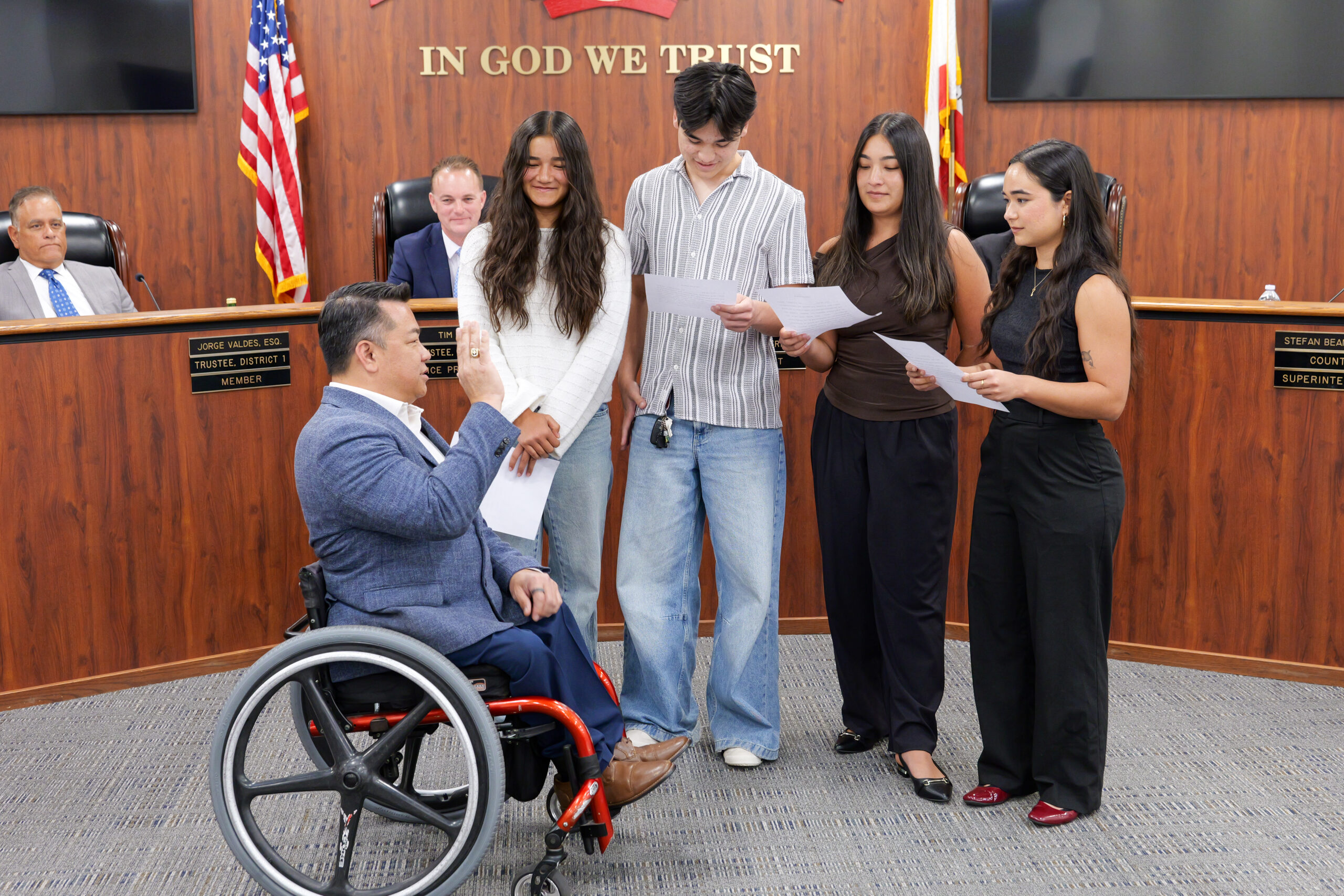 Dr. Stefan Bean raises his right hand while his four children administer the oath of office during an Orange County Board of Education meeting.