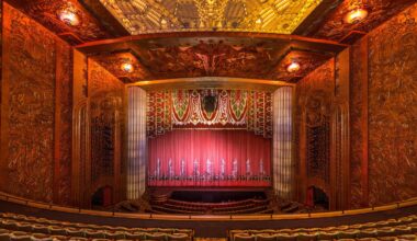 The inside of an ornate movie theater, shown from the balcony, with a large red curtain and seats