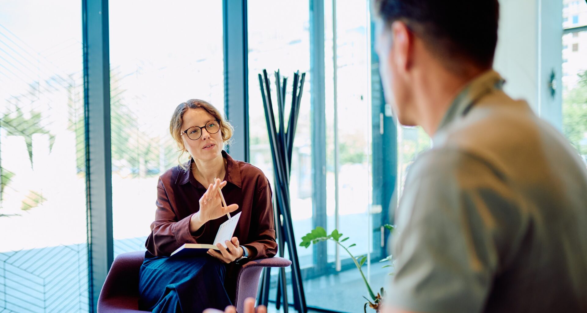 Female professional giving guidance and support to a man during a therapy session in a modern office setup