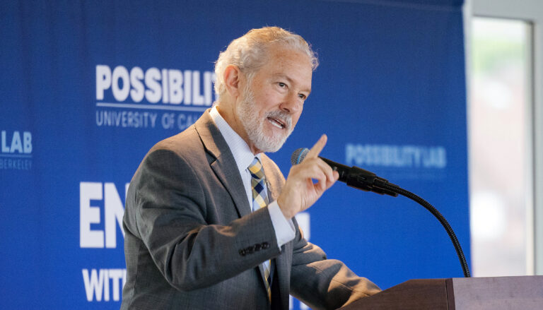 Chancellor Rich Lyons gestures as he speaks into a microphone, with a blue backdrop that features the Possibility Lab logo