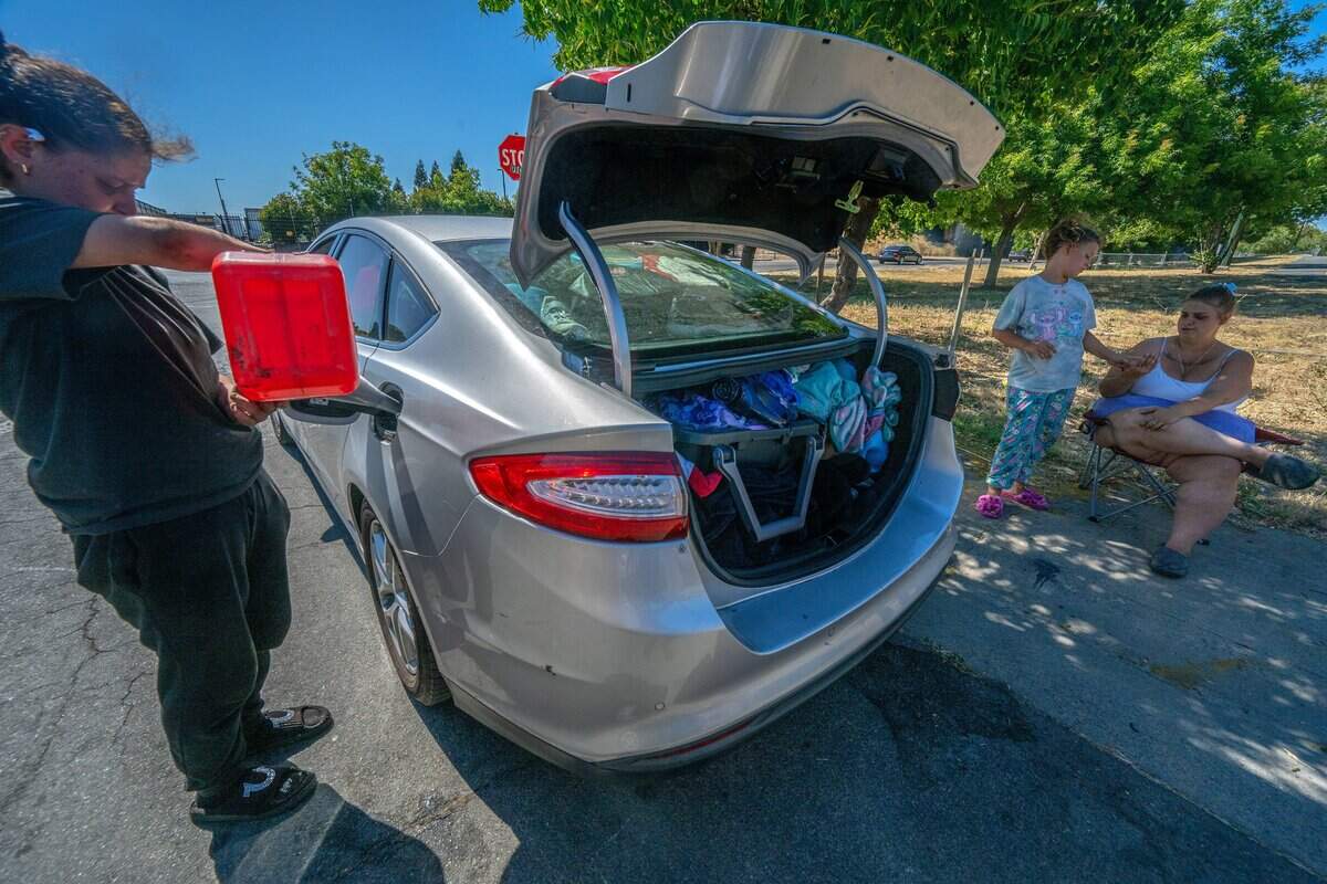 Tattiana Palaca, 35, and her daughter, Selena Palaca, 10, wait while a friend siphons gas into their car in Sacramento on Tuesday, June 30, 2026. The family — who are plaintiffs in a lawsuit against the City of Sacramento — lost their room in the city’s motel shelter program after changes to the program in June.