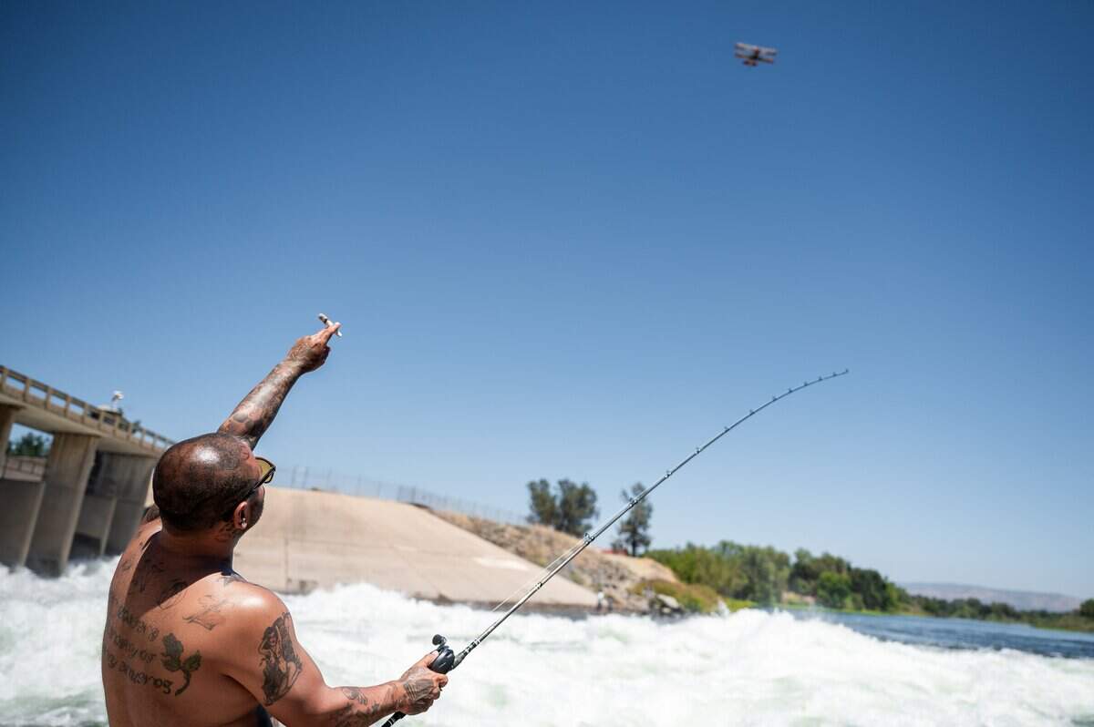 Ephraim Munoz points out an airplane flying by while fishing for salmon during the opening day of the salmon fishing season in Thermalito Afterbay Outlet in Oroville Wildlife Area in Oroville on Thursday, July 16, 2026.