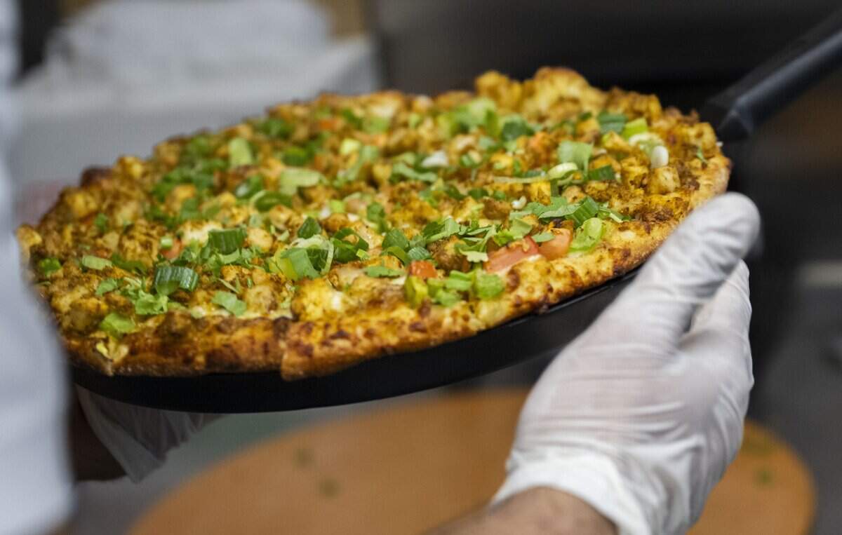 A Chicken Tikka pizza is pulled out of the oven during the grand opening of Tandoori Pizza at Sacramento's Downtown Commons on Wednesday, Oct. 15, 2025. The pizza includes a creamy garlic sauce, mozzarella cheese, red onions, diced tomatoes, chicken tikka, green onions and cilantro.