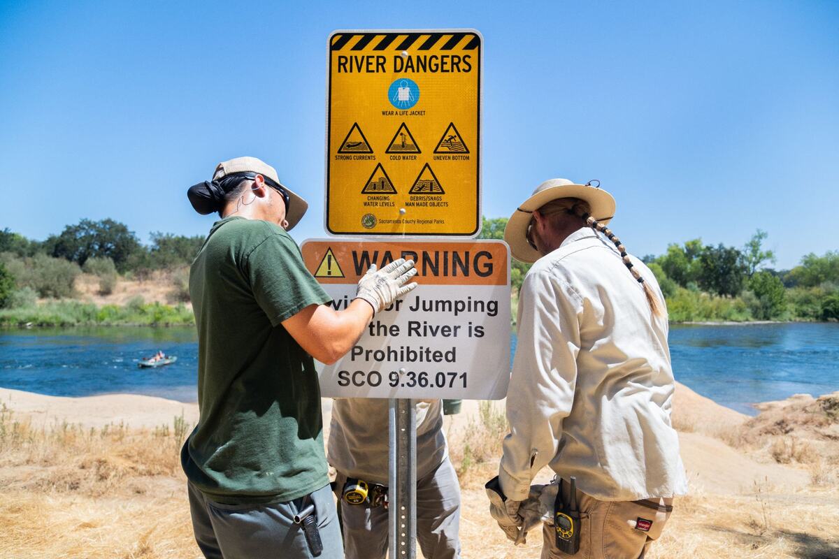 Park Maintenance workers Paul Rubio, left, Jason Roberson, back, and Andrew Stephens, right, install prohibiting diving and warning of river dangers near the Clay Banks along the American River in Rancho Cordova in 2024