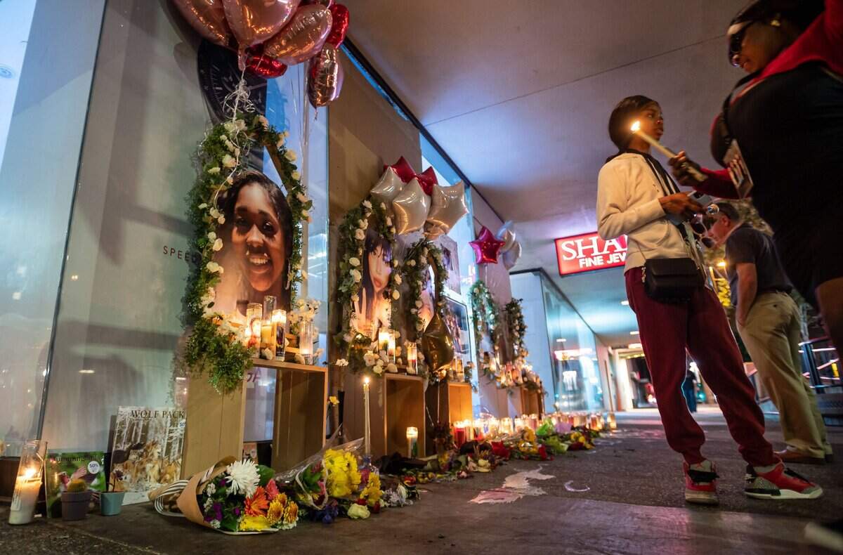 Valynda Cole, right of center, whose cousin Johntaya Alexander was one of the six people killed in the downtown Sacramento shooting early Sunday, stands next to a photo of her family member on the growing memorial for the victims Wednesday, April 6, 2022, on 10th and K streets in downtown Sacramento.