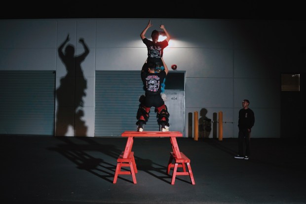 The Sun Hing lion tail dancer Bryan Huynh stands on the benches and lifts his lion head partner, Isabelle André, to stand on his legs. The team leader, Kevin Nguyen, right, watches and gives feedback on their movements, Wednesday, April 1, 2026, in San Jose, Calif. (Photo by Yu Wang)
