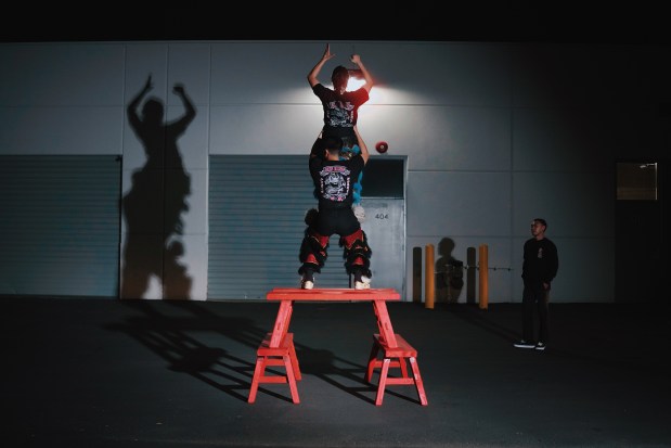 The Sun Hing lion tail dancer Bryan Huynh stands on the benches and lifts his lion head partner, Isabelle André, to stand on his legs. The team leader, Kevin Nguyen, right, watches and gives feedback on their movements, Wednesday, April 1, 2026, in San Jose, Calif. (Photo by Yu Wang)