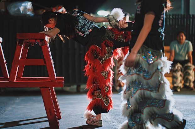 Sun Hing member Alicia Trinh stretches her legs on the bench during the practice outside the warehouse, Friday, April 17, 2026, in San Jose, Calif. (Photo by Yu Wang)