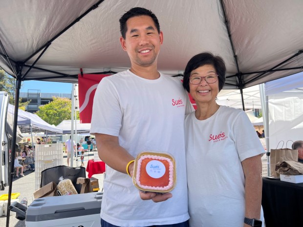 Darryl and Penny Tom pose with a mini guava cake at the Sue's Bites and Delights booth at San Jose's Japantown Farmers Market on June 14, 2026. (Photo by Grace Hwang Lynch)