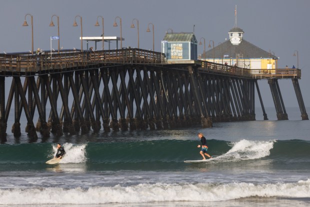 Imperial Beach resident Matt Henry rides a wave with his son Liam, 13, at the Imperial Beach Pier in March. (Kristian Carreon / The San Diego Union-Tribune)