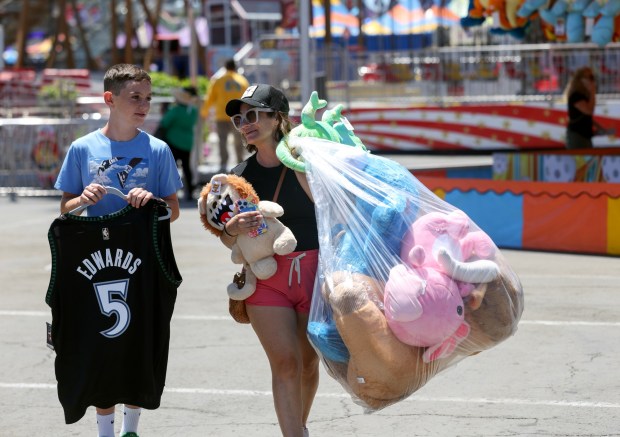 As they head for the exit, Lori MacLeod carries what her son Marco, 12, won as he carries a basketball shirt he received after playing the Take the Shot basketball game during the San Diego County Fair's final day in Del Mar on Sunday, July 05, 2026. MacLeod, from Phoenix, Ariz., said they always come to the San Diego County Fair on the last day because the game operators give them more prizes. (Hayne Palmour IV / For The San Diego Union-Tribune)