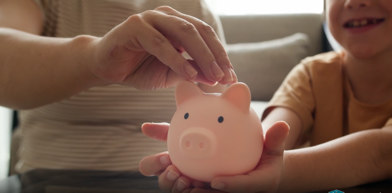 An adult and child place coins into a pink piggy bank, representing college and career savings opportunities available through the CalKIDS program.