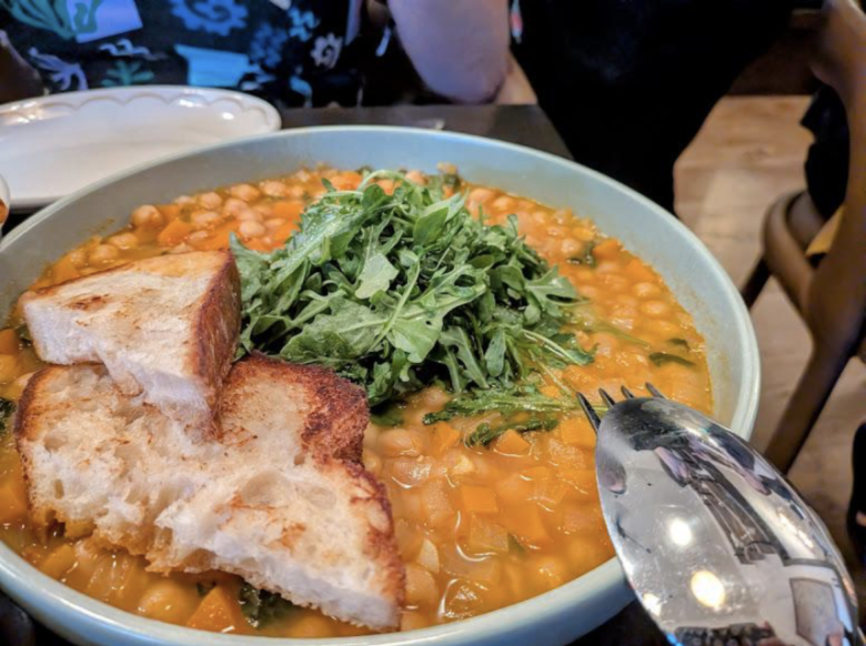 A bowl of vegetable and bean soup topped with fresh greens, served with two slices of toasted bread on the side.