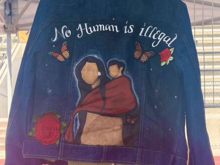 a jacket painted with the image of a mother and child with the words "No Human is Illegal"