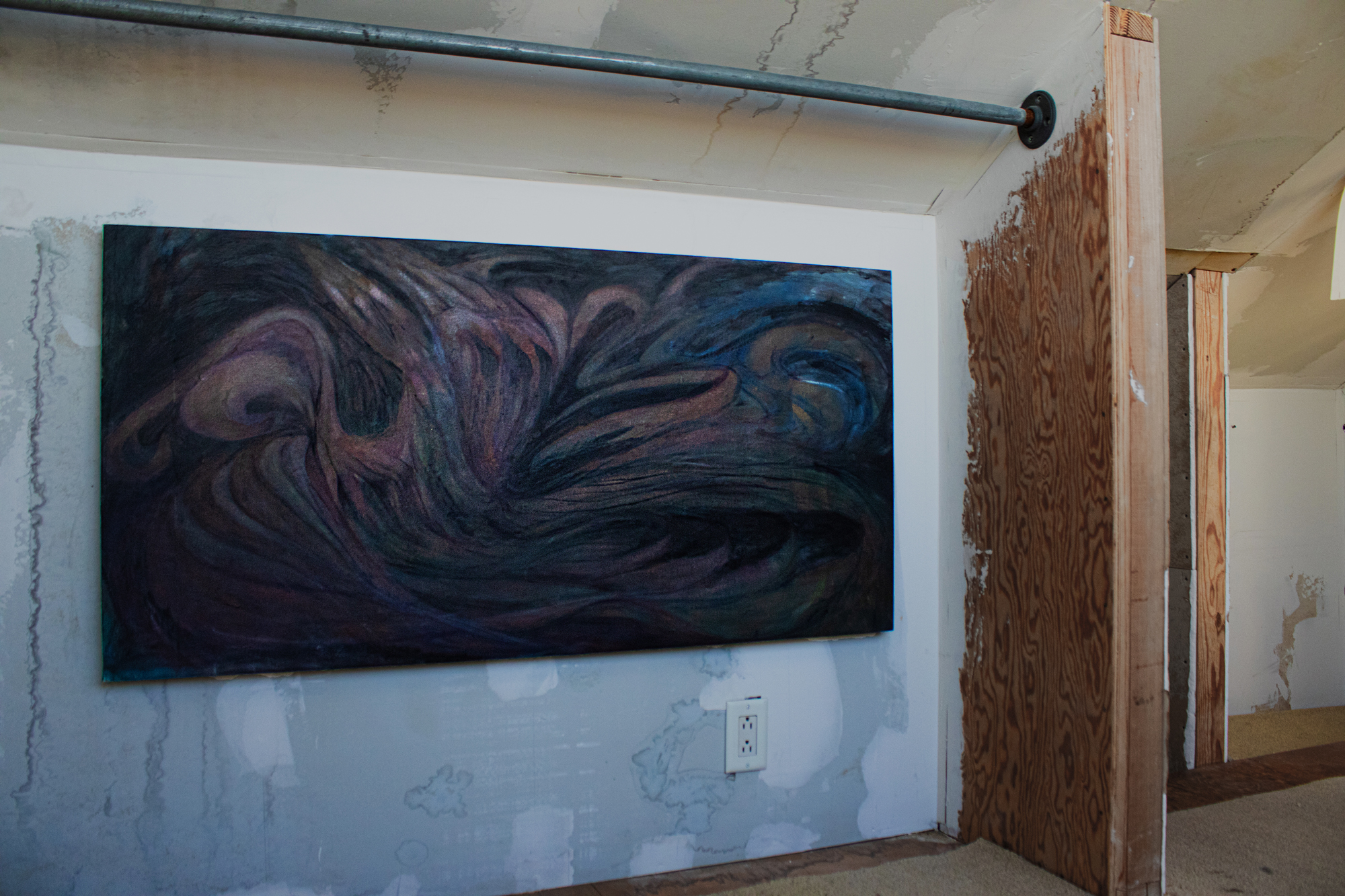 wide abstract painting hung on patched wall under low ceiling