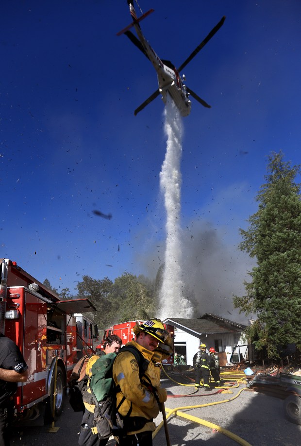Firefighters turn away from rotor wash debris kicked up by Cal Fire's Boggs Forest Helitack as the craft is used to help extinguish a house fire which nearly gutted the structure, Wednesday, Sept. 17, 2025, in Cazadero. The fire also spread in to vegetation, burning about 2.5 acres. (Kent Porter / The Press Democrat)