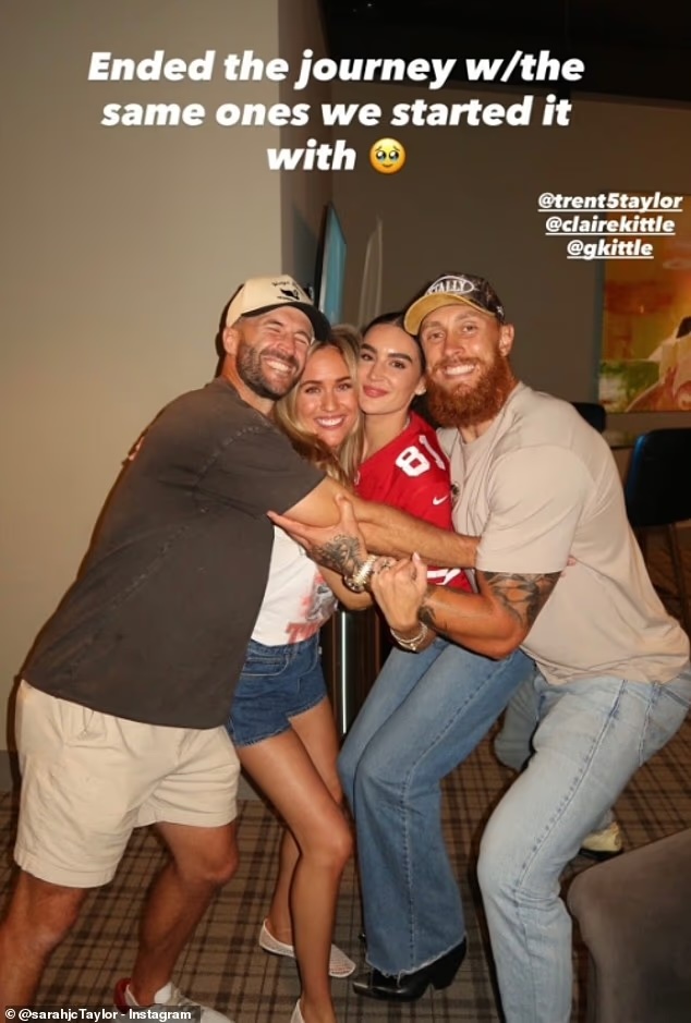 Four people embracing and smiling for a photo, with two men in hats and two women, one wearing a red jersey.