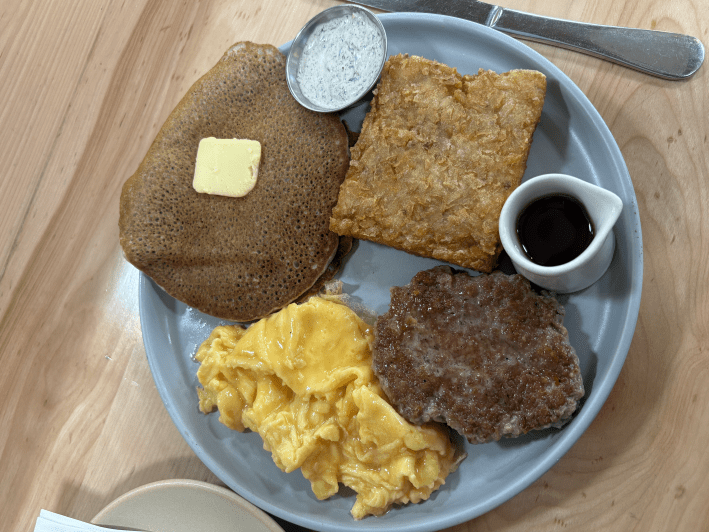 a plate with a pancake, sausage, eggs, and hashbrown