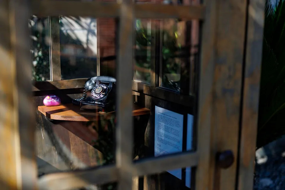 An old black rotary phone sits inside a wind phone booth.