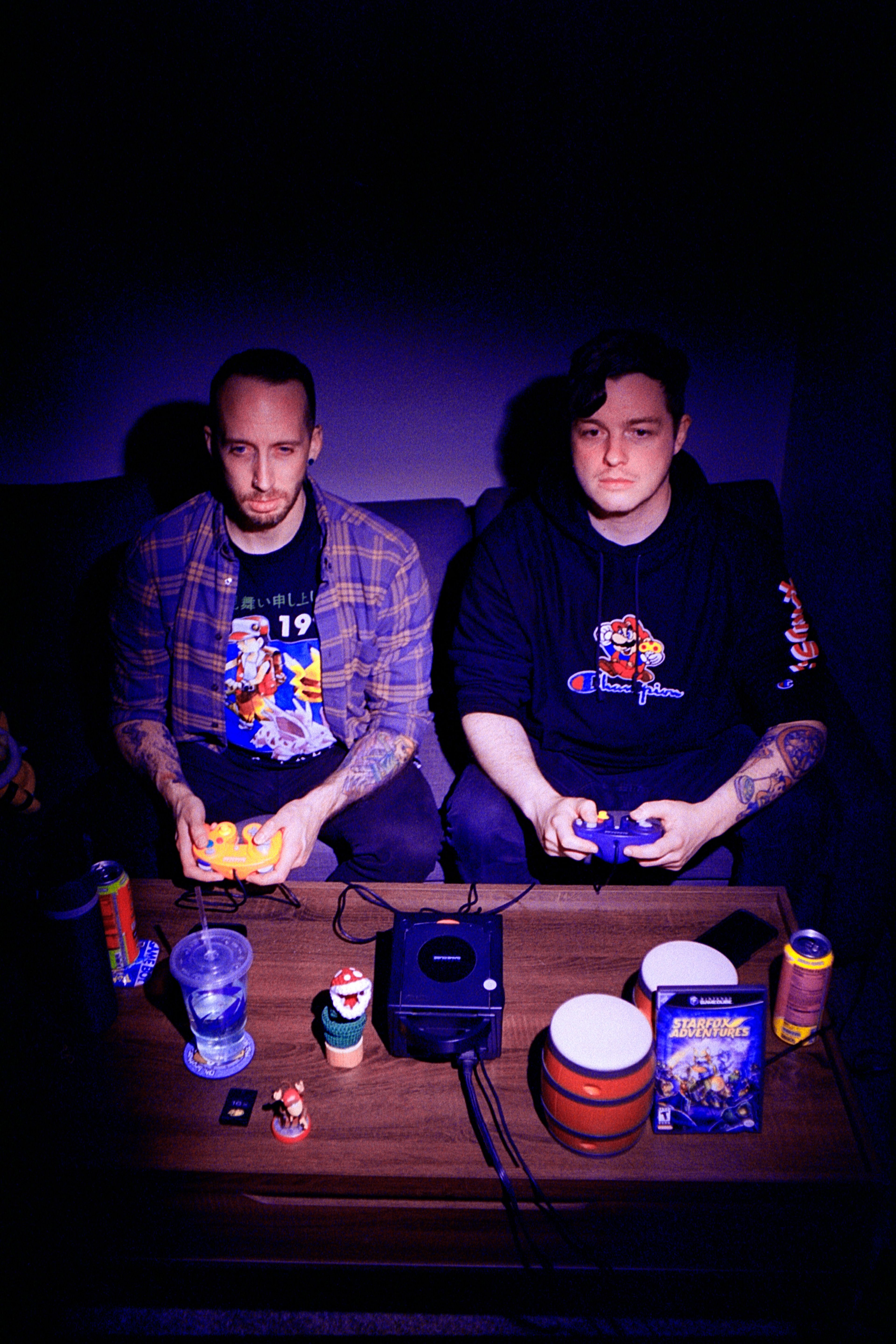 two men illuminated in a purple light stare into a screen while playing a game on the Nintendo Gamecube